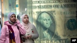 FILE - Egyptians walk past a poster depicting a U.S. dollar outside an exchange office in Cairo, Egypt, February. 9, 2023.