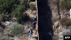 Пограничная стена, разделяющая США и Мексику. С левой (мексиканской) стороны видны люди, которые выбирают место для нелегального пересечения границы. Архивное фото.