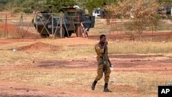 A Burkinabe soldier walks past a French Armoured Personnel Carrier part of a French military convoy heading to Niger, stopped by protesters in Kaya, Burkina Faso, Nov. 20, 2021.