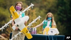 In this April 14, 2021, Girl Scouts Alice (right) and Gracie pose with a Wing delivery drone in Christiansburg, Va. The company is testing drone delivery of Girl Scout cookies in the area. (Sam Dean/ Wing LLC via AP)