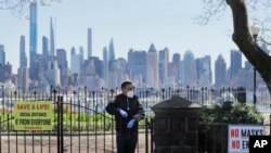 A public safety officer stands behind the gates of a temporarily closed park at a viewing point for a flyover of the New York City skyline by the U.S. Navy Blue Angels and U.S. Air Force Thunderbirds in Weehawken, New Jersey, April 28, 2020.