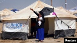 A woman, who fled from violence in Mosul, carries a baby in a camp edging Irbil in Iraq's Kurdistan region June 25, 2014. 