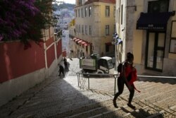 In this photo taken June 24, 2020, a woman wearing a face mask walks past workers washing the street in Lisbon's old center.