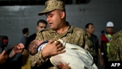 A soldier holds a baby as Turkish citizens evacuated from Lebanon disembark from the TCG Bayraktar war ship after its arrival at the southern Turkish port of Mersin on Oct. 10, 2024.