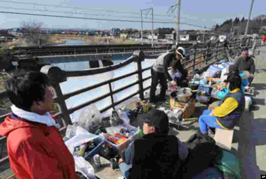 Local residents shelter on a road side of a bridge in Tagajo, Miyagi prefecture on March 13, 2011.