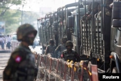 Tentara berdiri di samping kendaraan militer ketika warga berkumpul untuk memprotes kudeta militer, di Yangon, Myanmar, 15 Februari 2021. (Foto: Reuters)