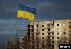 Bendera nasional Ukraina berkibar di dekat bangunan yang dihancurkan oleh serangan militer Rusia, di Kota Borodianka, di wilayah Kyiv, Ukraina 15 Februari 2023. (Foto: REUTERS/Gleb Garanich)