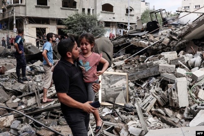 Một người đàn ông bế đứa trẻ đang khóc khi đi trước tòa nhà bị phá hủy trong cuộc không kích của Israel ở Thành phố Gaza vào ngày 7 tháng 10 năm 2023.
