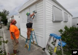 Chris Nagiewicz, left, watches as his wife, Mary, screws in a hurricane panel, Aug. 1, 2020, on a trailer home in Briny Breezes, Fla. Hurricane Isaias was headed toward the Florida coast.