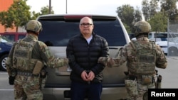 Oficiales de policía del Servicio de Inmigración y Control de Aduanas de Estados Unidos sostienen al capo de la droga Osiel Cárdenas Guillén, quien fue deportado y entregado a las autoridades mexicanas en Tijuana el 16 de diciembre de 2024