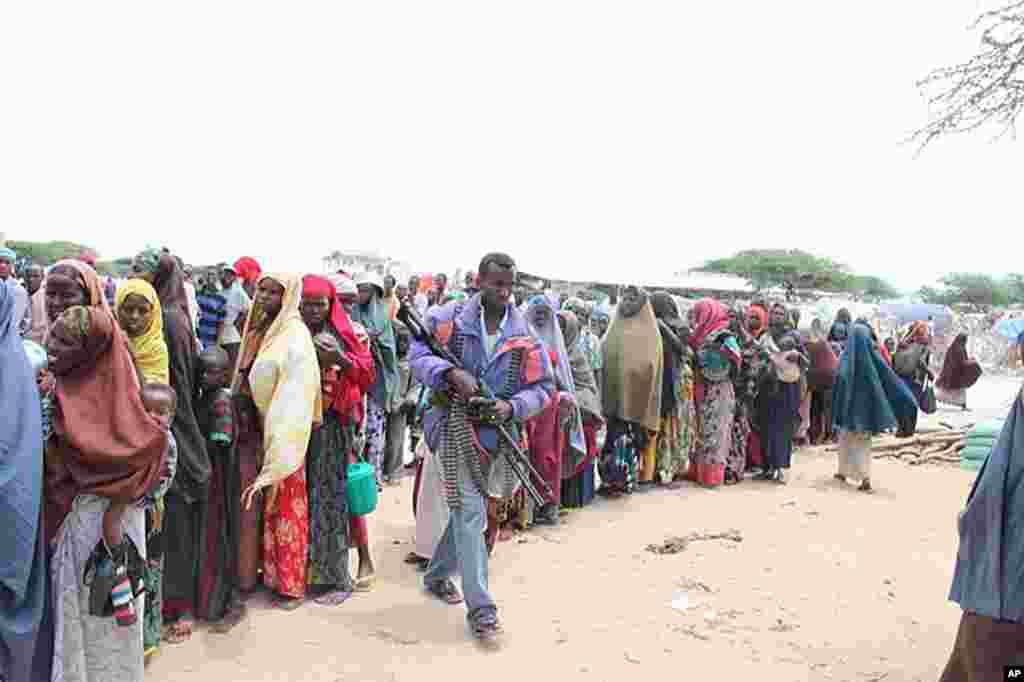 Gunman walks through line of women waiting for ration at Badbaado IDP camp in Mogadishu, Somalia, August 11, 2011. (VOA - P. Heinlein)