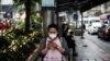 FILE - A woman, wearing a face mask, uses her mobile phone while waiting at a bus stop in Bangkok, Thailand, Jan. 30, 2019.