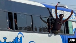 Um homem gesticula com uma bandeira dentro de um autocarro enquanto as pessoas deslocadas pela guerra em curso no Sudão regressam a Wad Madani, no estado de Jazira, a 6 de fevereiro de 2025, depois de a cidade ter sido retomada pelo exército sudanês