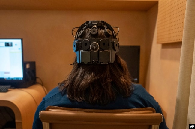 Emily Hollenbeck, a deep brain stimulation therapy patient, demonstrates an EEG device that records brain activity as she reacts to short videos at Mount Sinai’s “Q-Lab” in New York on Dec. 20, 2023. (AP Photo/Mary Conlon)