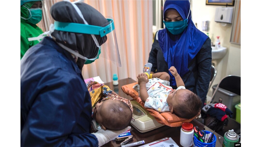 Tenaga medis dengan APD bersiap memberikan vaksin tuberkulosis dan vaksin polio oral untuk bayi di Puskesmas Surabaya, 30 Juni 2020. (Foto: AFP/Juni Kriswanto)