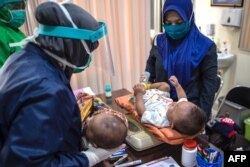 Tenaga medis dengan APD bersiap memberikan vaksin tuberkulosis dan vaksin polio oral untuk bayi di Puskesmas Surabaya, 30 Juni 2020. (Foto: AFP/Juni Kriswanto)
