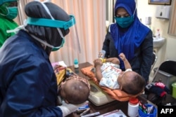 Petugas medis dengan APD bersiap memberikan vaksin tuberkulosis dan vaksin polio oral untuk bayi di Puskesmas Surabaya, 30 Juni 2020. (Foto: AFP)