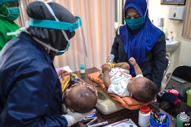 FILE - Medical staff clad in protective gear prepare to administer the vaccine for tuberculosis and oral polio for babies at a community health center in Surabaya, Indonesia, June 30, 2020.