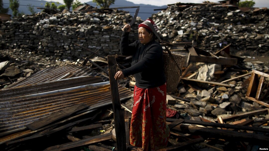 An earthquake victim cuts wood from the debris of her house in Barpak village, the epicenter of the April 25 earthquake in Nepal.