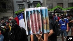 Anti-government protester hold a sign with the portraits of the Chile's President Sebastian Pinera and late military dictator Gen. Augusto Pinochet, during a protest in Santiago, Chile, Nov. 18, 2019. 