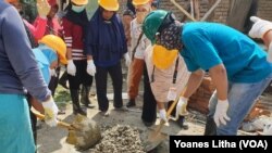 Seorang pelatih (baju biru), memandu dua orang ibu mempraktekkan cara membuat adukan semen untuk pengecoran tiang bangunan rumah, 7 Desember 2019. (Foto: VOA/Yoanes Litha)