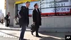 Men walk past an electronic stock indicator of a securities firm in Tokyo, Jan. 31, 2017.