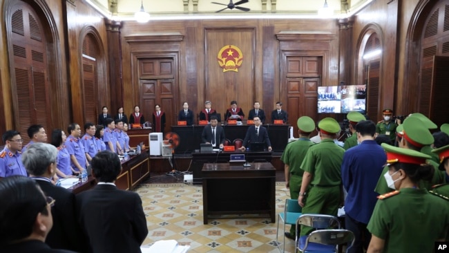 People stand before Vietnamese real estate tycoon Truong My Lan enters a courtroom in Ho Chi Minh City, Vietnam on Tuesday, March 5, 2024. (Phan Thanh Vu/VNA via AP)