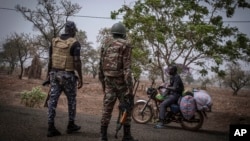 FILE - A Beninese police officer and soldier stop a motorcyclist at a checkpoint outside Porga, Benin, March 26, 2022. 