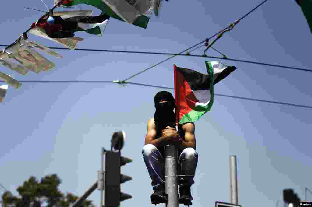 A masked Palestinian youth looks on from atop a pole during the funeral of 16-year-old Mohammed Abu Khudair in Shuafat, an Arab suburb of Jerusalem, July 4, 2014.