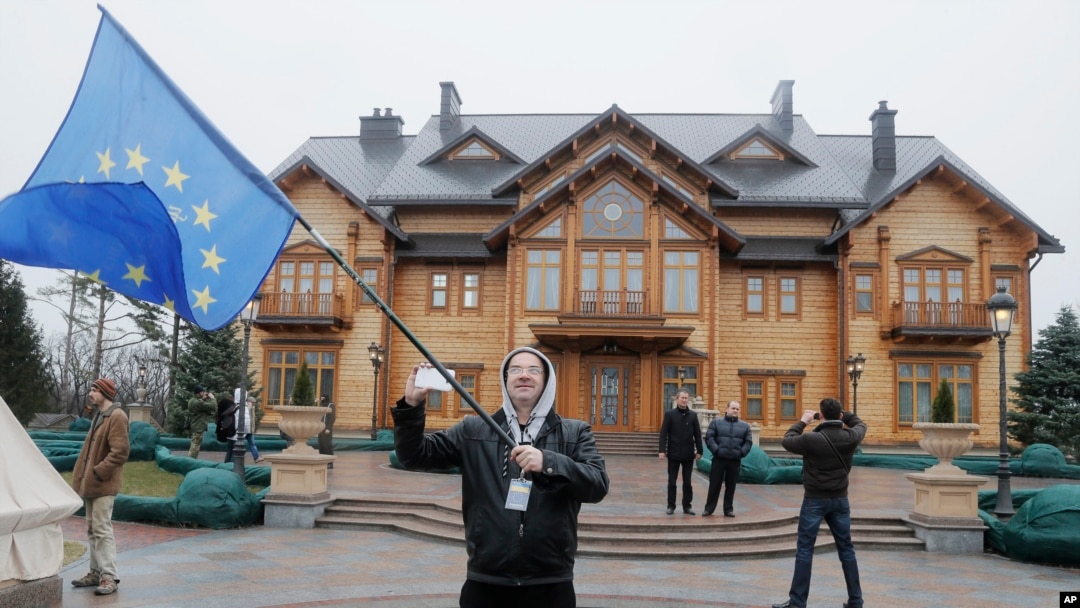 Seorang demonstran mengibarkan bendera Ukraina di depan tempat kediaman Presiden Yanukovych di Mezhyhirya, 20 kilometer dari ibukota Kyiv, Ukraina, Sabtu (22/2). Petugas keamanan dan relawan menjaga tempat kediaman yang telah ditinggalkan penghuninya ini, untuk menghindari terjadinya pengrusakan dan penjarahan.
