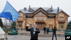 Seorang demonstran mengibarkan bendera Ukraina di depan tempat kediaman Presiden Yanukovych di Mezhyhirya, 20 kilometer dari ibukota Kyiv, Ukraina, Sabtu (22/2). Petugas keamanan dan relawan menjaga tempat kediaman yang telah ditinggalkan penghuninya ini, untuk menghindari terjadinya pengrusakan dan penjarahan.