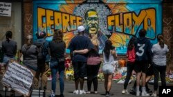 FILE - People are seen gathered at a memorial featuring a mural of George Floyd, near the spot where he died while in police custody, in Minneapolis, Minnesota, May 31, 2020.
