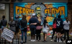 FILE - People are seen gathered at a memorial featuring a mural of George Floyd, near the spot where he died while in police custody, in Minneapolis, Minnesota, May 31, 2020.