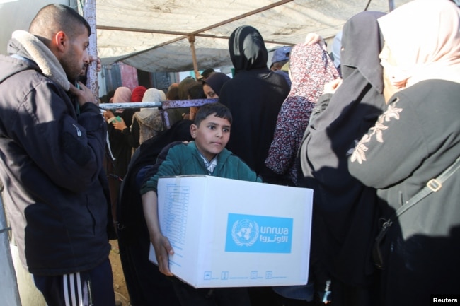 Seorang anak laki-laki Palestina membawa kotak bantuan yang disediakan oleh UNRWA, menyusul gencatan senjata antara Israel dan Hamas, di Khan Younis di Jalur Gaza selatan, 21 Januari 2025. (Hatem Khaled/REUTERS)