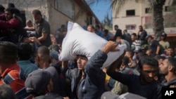 FILE - Palestinians gather to receive bags of flour distributed by UNRWA, the U.N. agency helping Palestinian refugees, in Deir al-Balah, central Gaza Strip, Nov. 2, 2024.