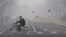 FILE - A man rides an electric bike crossing a street shrouded by haze in Beijing.