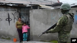 Un saldado captado en uno de los vecindarios en las afueras de Quito, Ecuador como parte de los despliegues de seguridad ordenados por el Gobierno para hacer frente a la ola de violencia. Una niña y su madre observan desde una humilde vivienda.