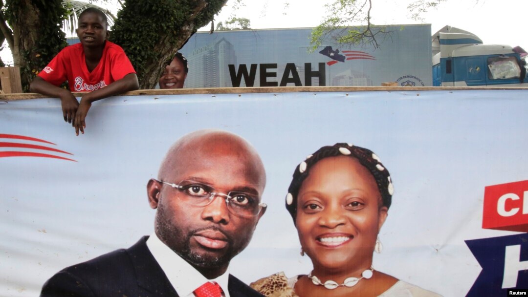 Pendukung mantan pemain sepak bola dan kandidat presiden Kongres untuk Perubahan Demokrasi, George Weah, berdiri di belakang spanduk kampanye presiden di Monrovia, Liberia. 