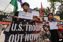 Demonstrators carry placards and shout slogans during a rally in front of Camp Aguinaldo military headquarters in Quezon City, Philippines on Tuesday, April 11, 2023 as they protest against opening ceremonies for the joint military exercise flag called "Balikatan."