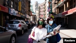 FILE - Shirley Ng (l) , a volunteer with the Chinatown Block Watch neighborhood patrol group, distributes Chinese newspaper along a street in Chinatown during the outbreak of the coronavirus disease (COVID-19) in New York City, New York, May 17, 2020.