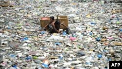 A father and son (C) on a makeshift boat made from styrofoam paddle through a garbage filled river as they collect plastic bottles that they can sell in junkshops in Manila on March 19, 2015. They earn three US dollars a day. The Philippines will be obser