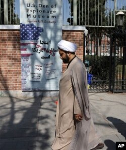 FILE - A Shi'ite Muslim cleric walks past anti-U.S. graffiti on the wall of the former U.S. Embassy, in Tehran, Iran, Oct. 15, 2019.