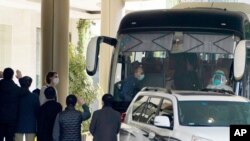 Para petugas melambaikan tangan mereka ke tim ahli dari Organisasi Kesehatan Dunia (WHO) yang mengakhiri karantina mereka dan bersiap untuk meninggalkan hotel karantina dengan bus di Wuhan di provinsi Hubei China tengah, Kamis, 28 Januari 2021. (Foto AP / Ng Han Guan)
