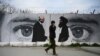 FILE - A man walks by a wall painted with images of U.S. Special Representative for Afghanistan Reconciliation Zalmay Khalilzad, left, and Taliban co-founder Mullah Abdul Ghani Baradar, in Kabul, April 5, 2020.