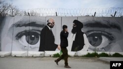 Seorang pria melintas di depan mural bergambar Utusan Khusus AS untuk Afghanistan Zalmay Khalilzad (kiri) dan pendiri Taliban, Mullah Abdul Ghani Baradar, di Kabul, 5 April 2020.