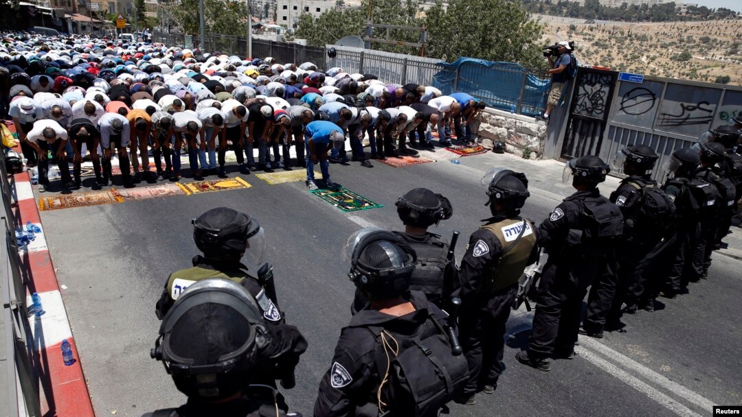 Warga Palestina melakukan shalat Jumat, sementara polisi Israel melakukan penjagaan di pinggiran Yerusalem (4/7). 