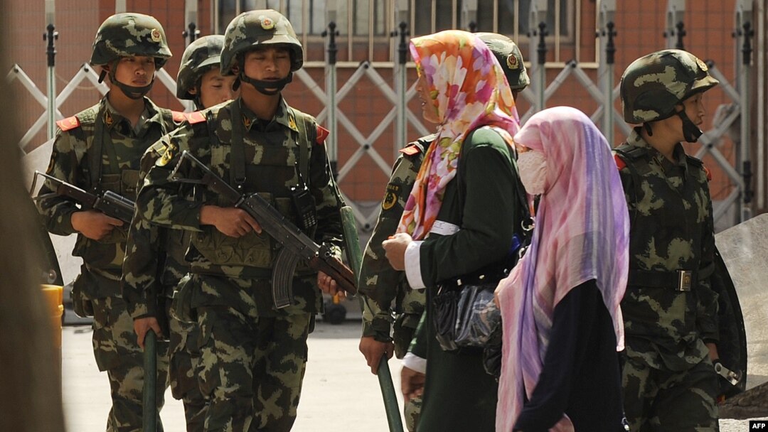 Perempuan etnis Muslim Uighur melewati polisi paramiliter China yang sedang berpatroli di sebuah jalan di Urumqi, ibu kota wilayah Xinjiang China pada 3 Juli 2010. (Foto: AFP)
