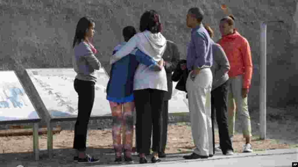 Malia Obama, Sasha Obama, first lady Michelle Obama, and Ahmed Kathrada a former prisoner with Mandela, stand in the courtyard of the prison on Robben Island.