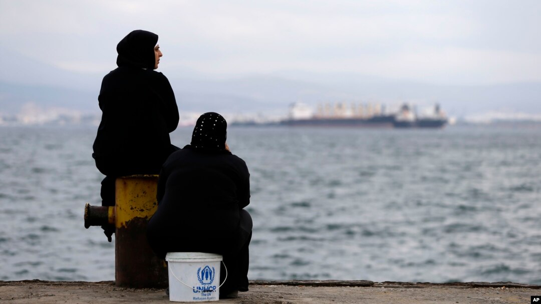 FILE - Two women sit on a dock of a refugee camp which houses about 3,200 refugees and migrants, in the western Athens suburb of Skaramagas, Aug. 25, 2016. 