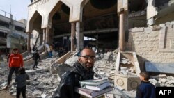 Čovjek hoda sa spašenim vjerskim knjigama dok ljudi pregledavaju štetu u ruševinama džamije nakon izraelskog bombardiranja, u Rafi, u južnom pojasu Gaze 12. februara 2024.